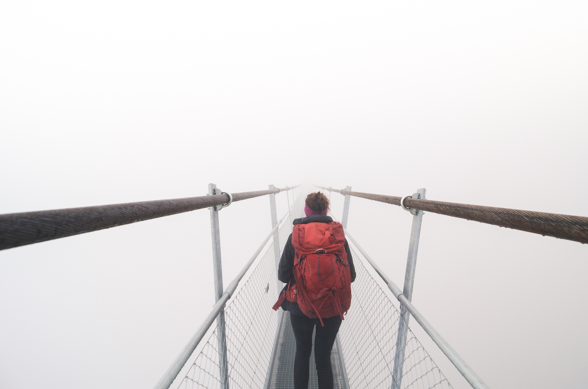 Female tourist walking across a suspension bridge in heavy fog